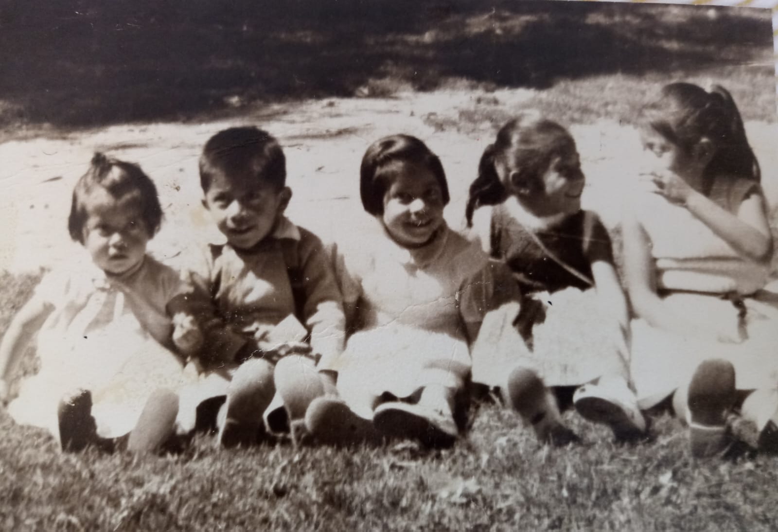 Fotografía antigua de cinco niños sentados juntos al aire libre.